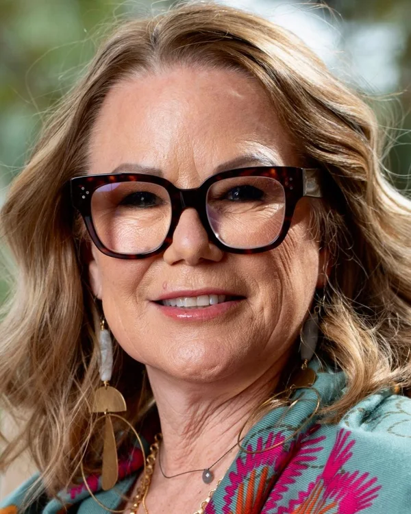 Chaille DeFaria, smiling, in tortoiseshell glasses and a teal floral scarf